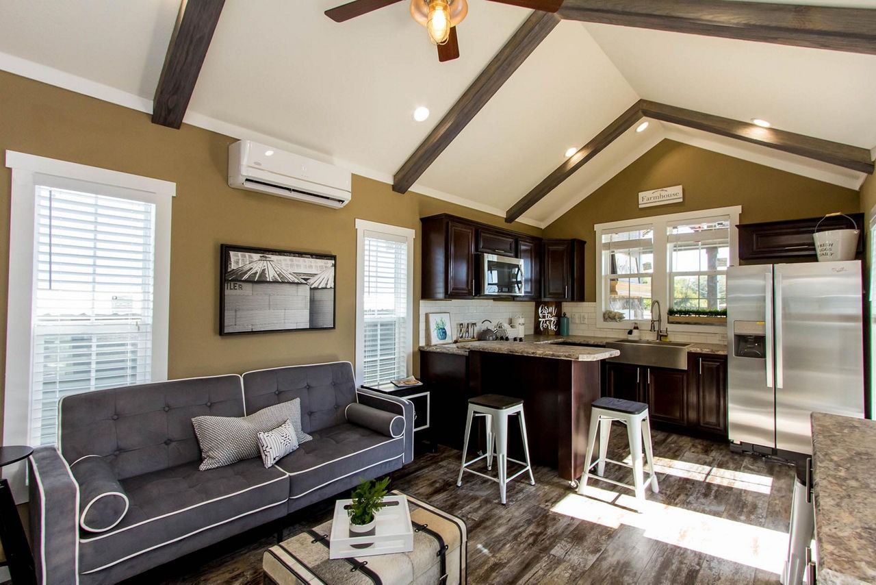 Bright kitchen and living area with gray sofa, bar stools, stainless fridge, and vaulted wood-beam ceiling