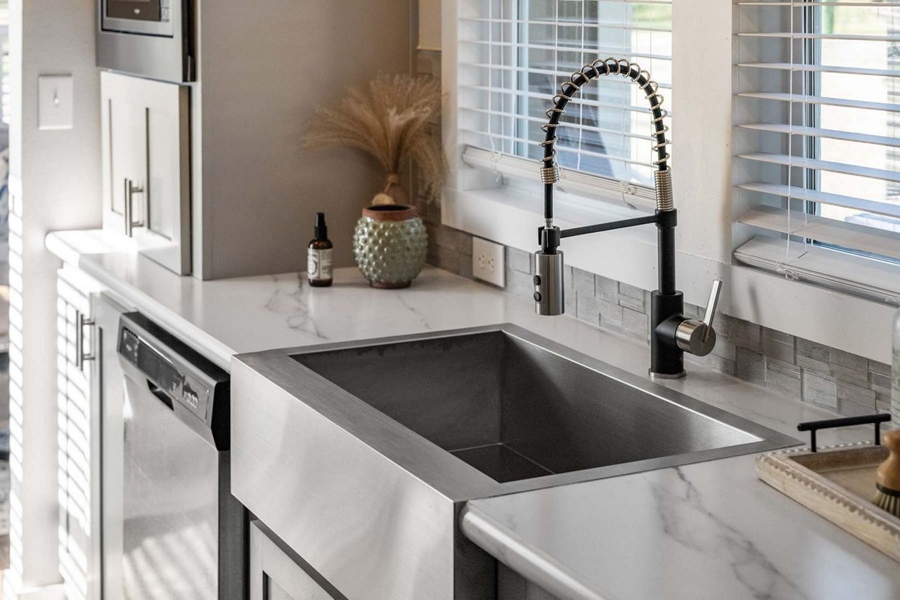 Modern kitchen with stainless steel sink, faucet, dishwasher, and countertop decor by a window