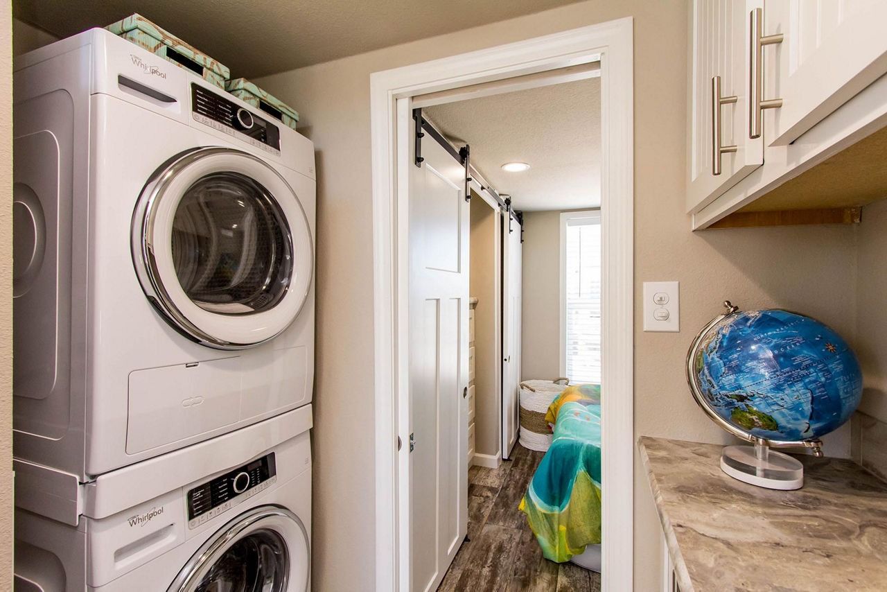 Laundry room with stacked washer and dryer, hallway, and countertop with a blue globe.