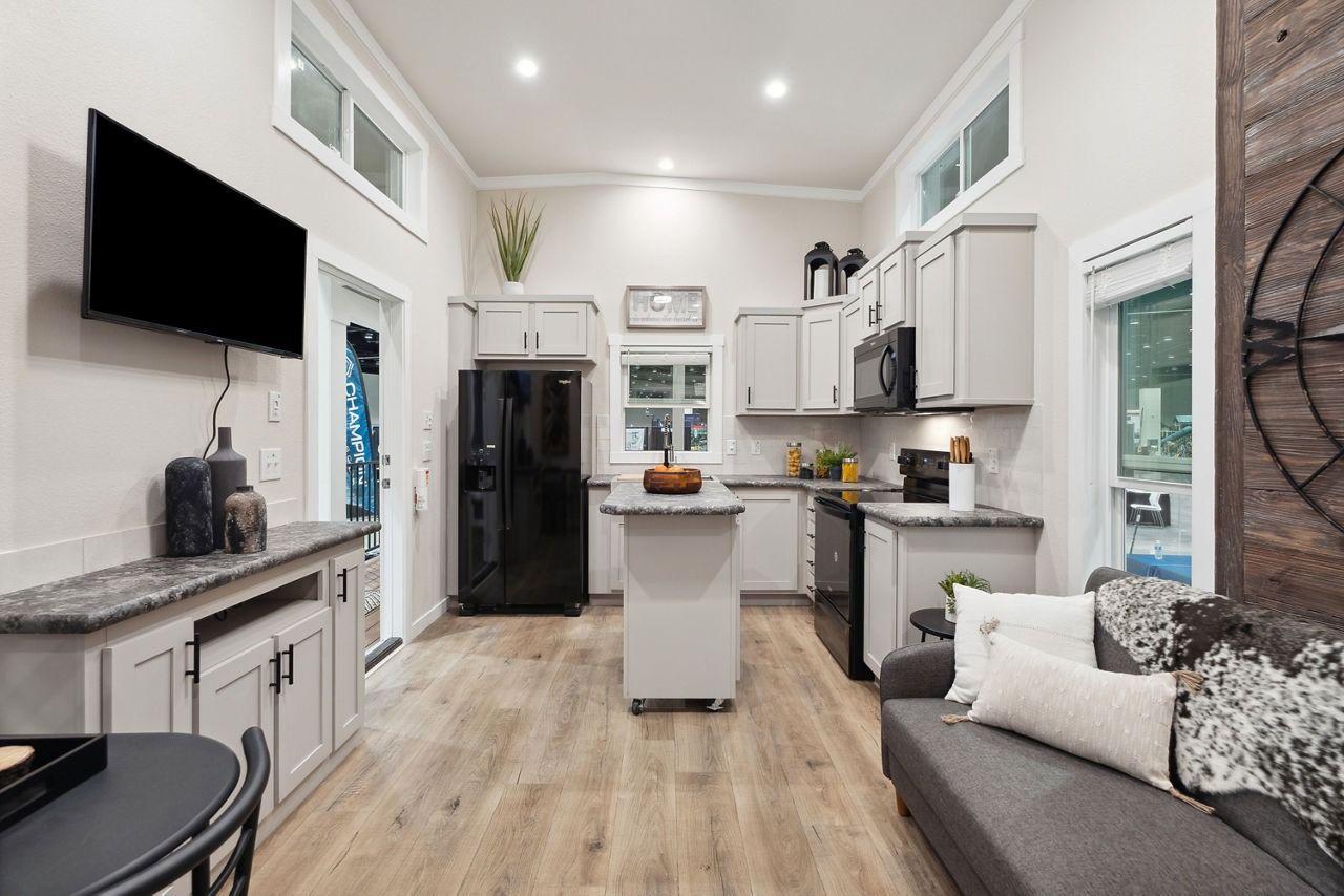 Bright modern kitchen with white cabinets, black appliances, island, and gray sofa in a loft space