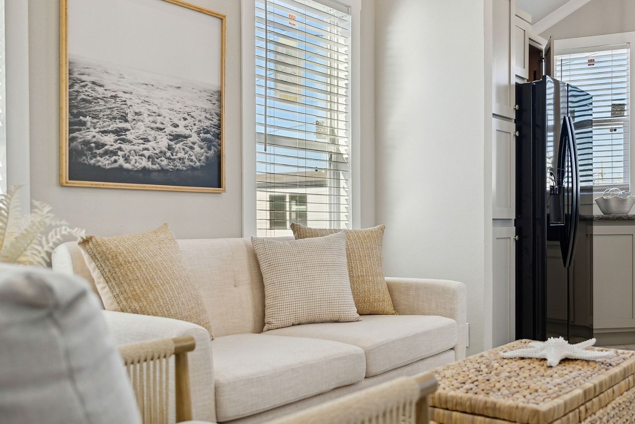 Bright living room with beige sofa, woven ottoman, framed art, and large windows with blinds