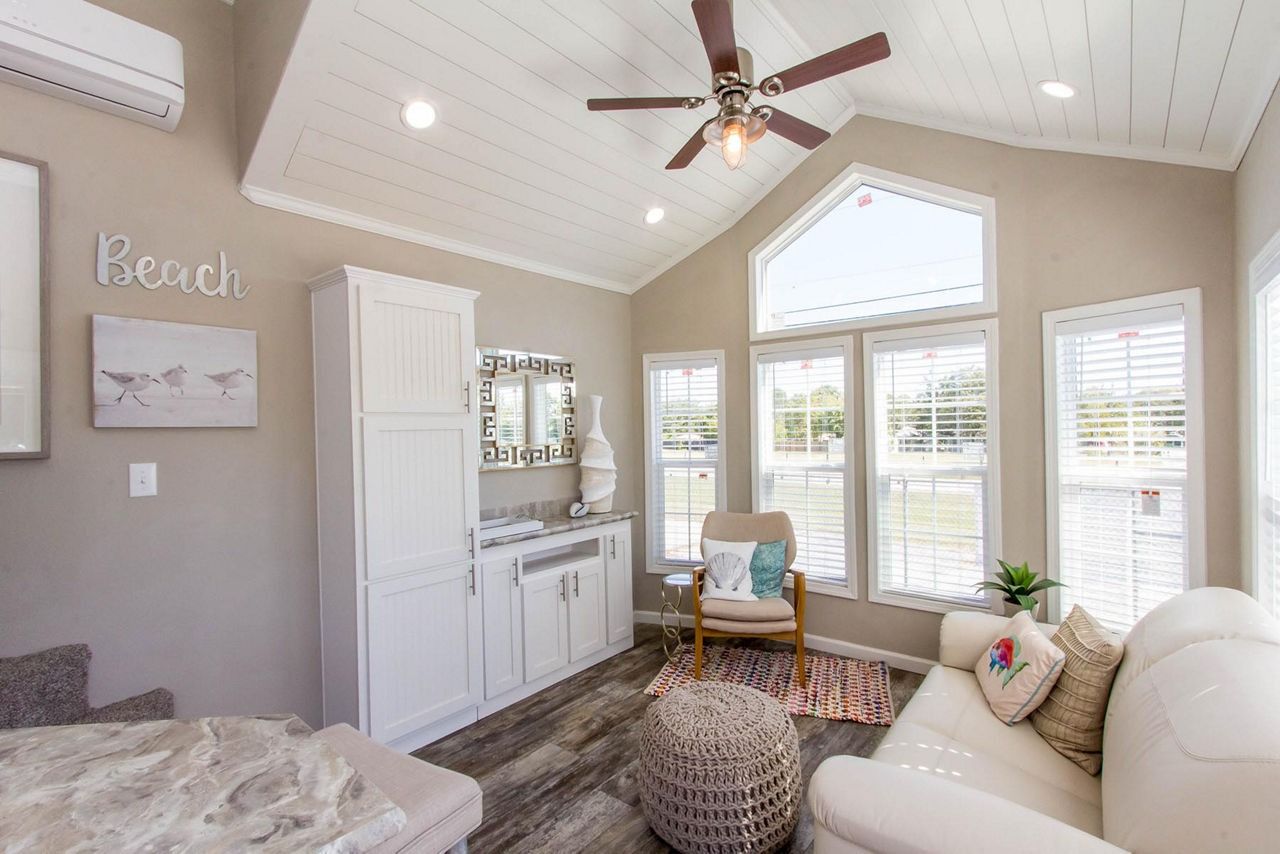 Bright sunroom with white furniture, vanity, ceiling fan, and large windows overlooking greenery