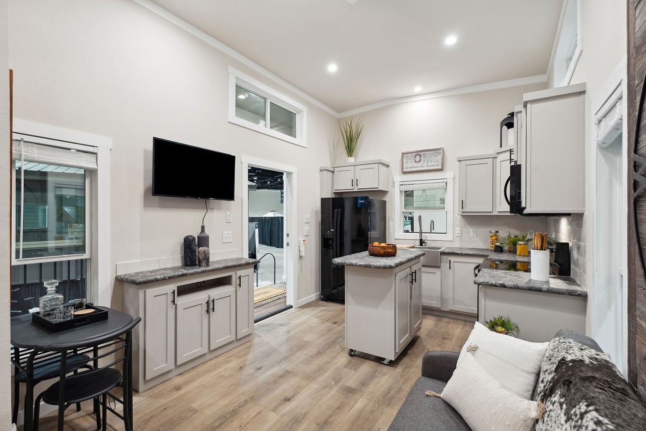 Bright modern kitchen and living area with white cabinets, island, TV, and sofa.