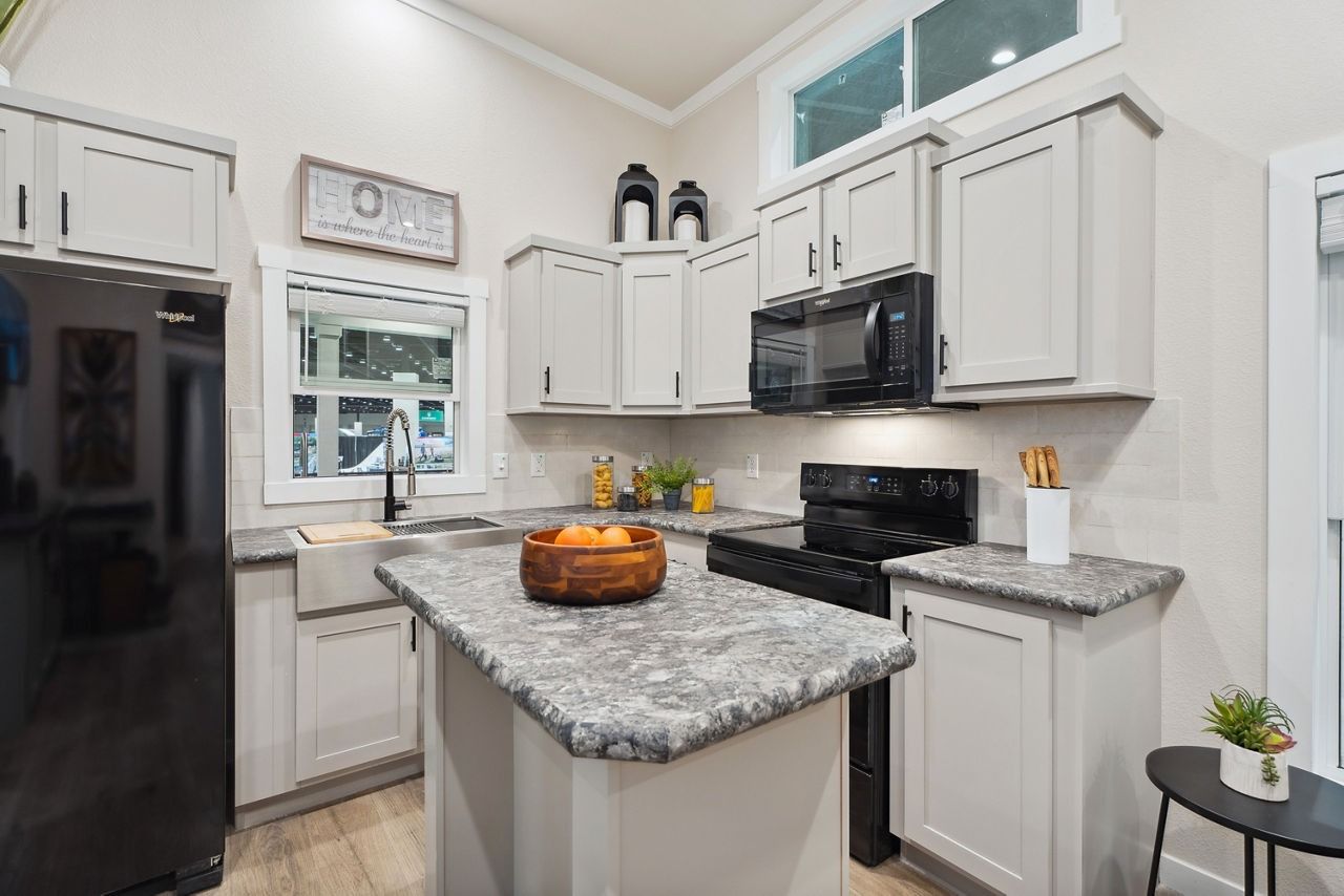 Bright white kitchen with granite island, black appliances, and pumpkin centerpiece.