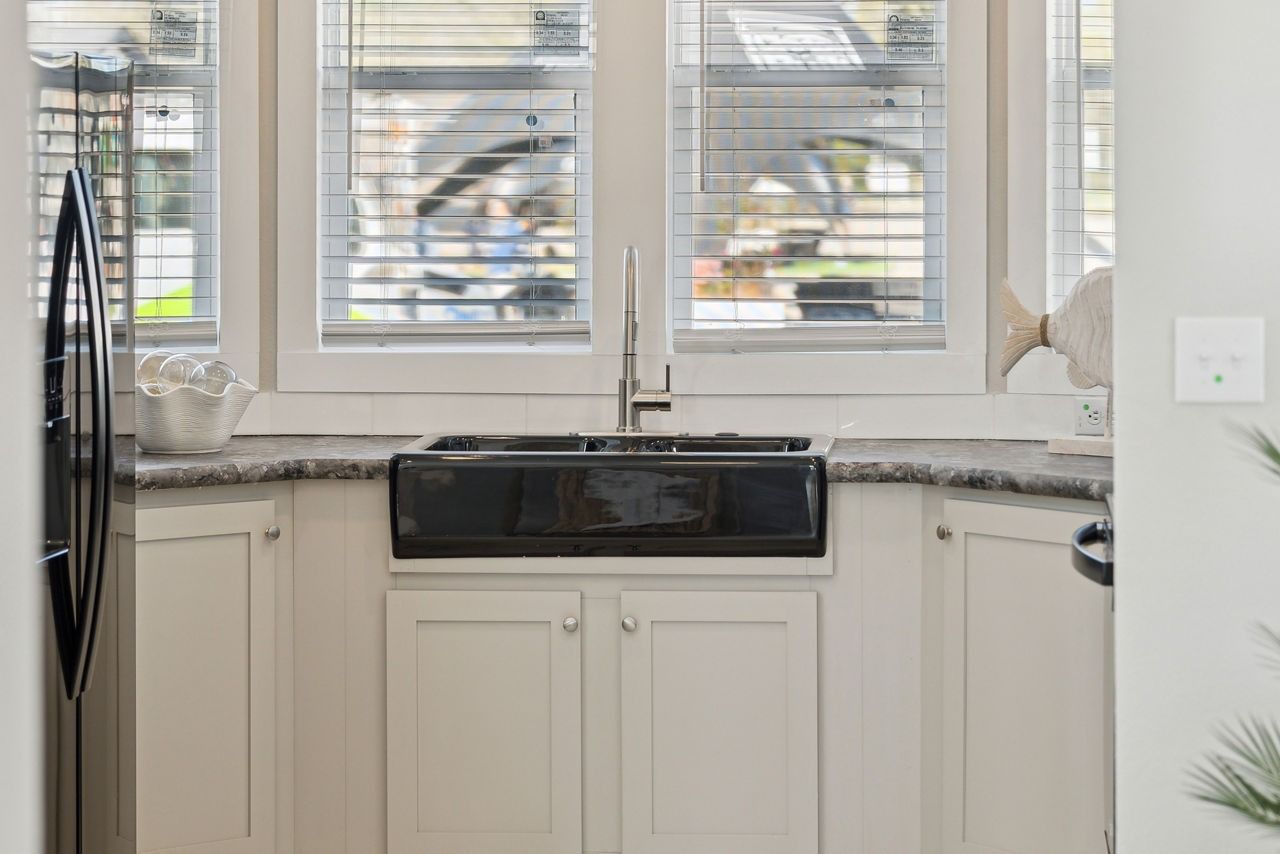 Bright kitchen sink under a window with white blinds and granite countertop