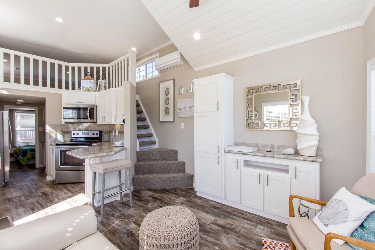 Bright open living room with kitchen, staircase, white cabinets, and gray rug in a modern home