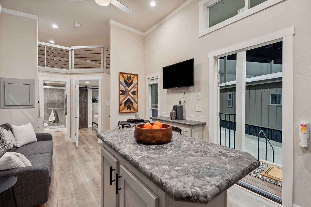 Modern open-plan living room with gray sectional, island countertop, wall TV, and sliding glass doors