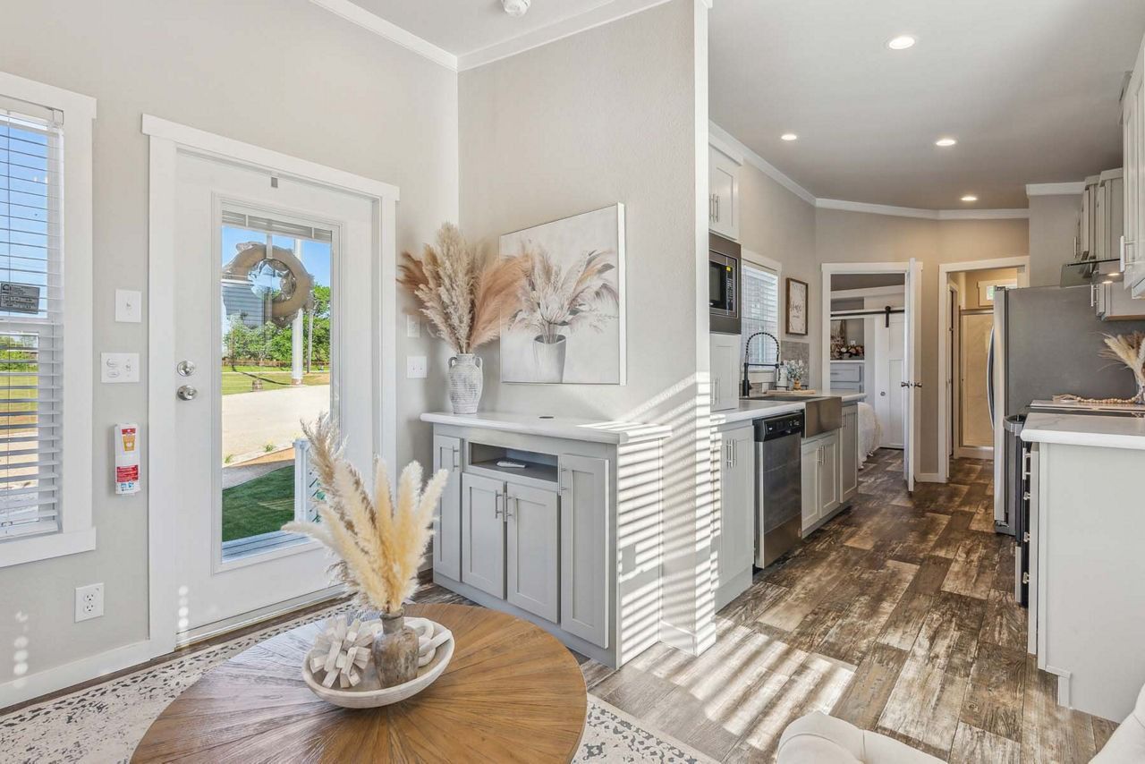 Bright entryway with wood floors, front door, console table, and open hallway into a modern kitchen