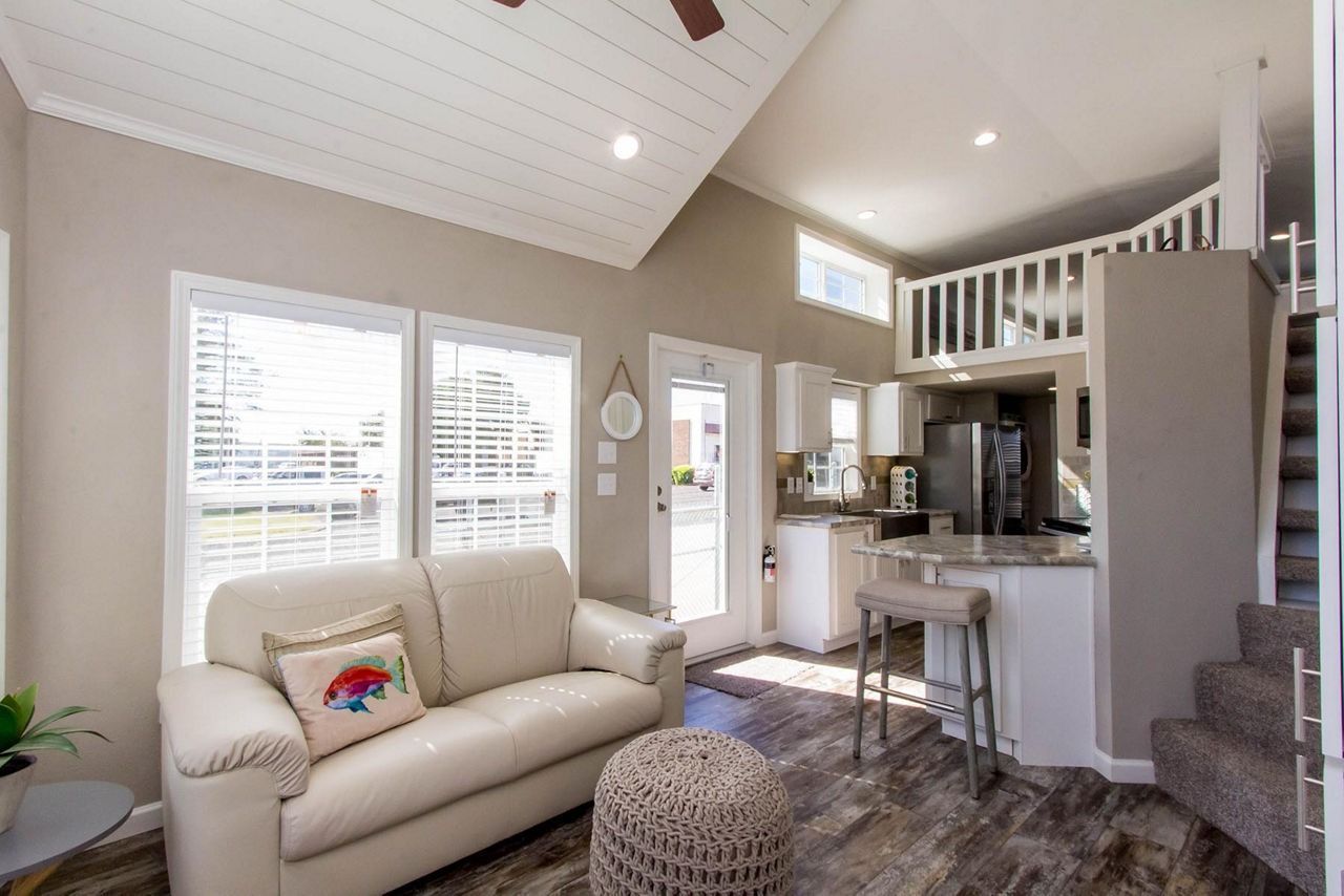 Cozy living room with white sofa, high ceiling, staircase, and loft view in bright natural light