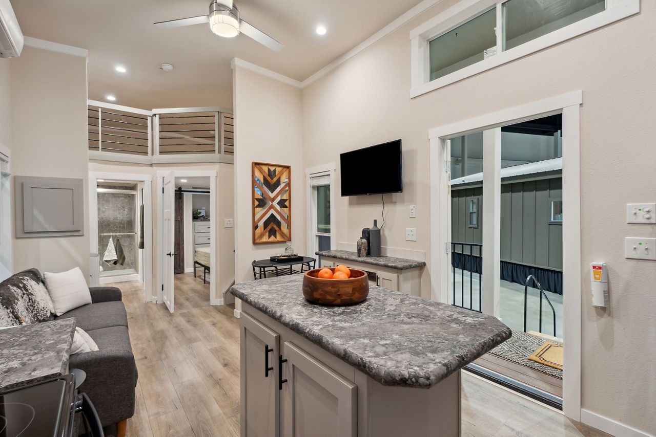 Modern open-plan kitchen and living room with gray island, wall-mounted TV, and sliding glass door