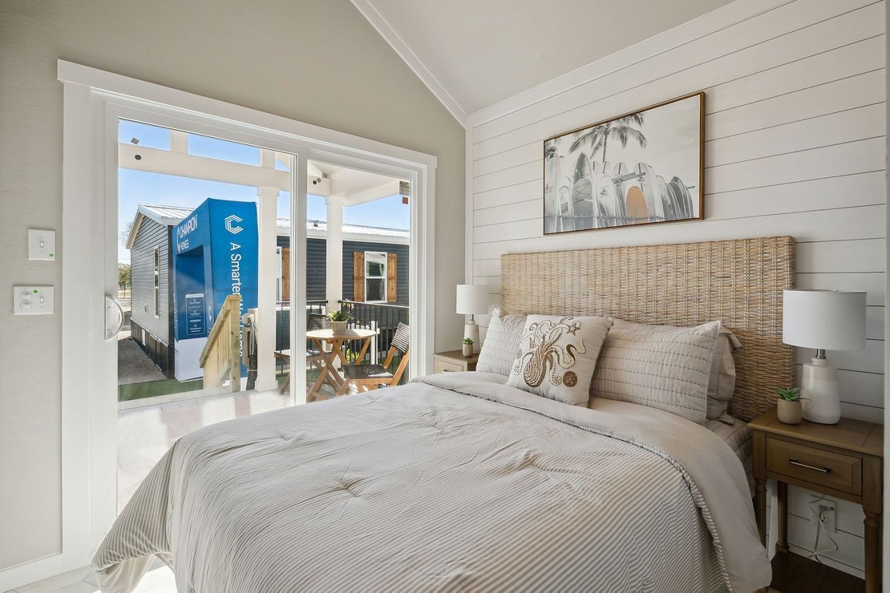 Bright bedroom with woven headboard, white bedding, and a glass door opening to a patio outside.