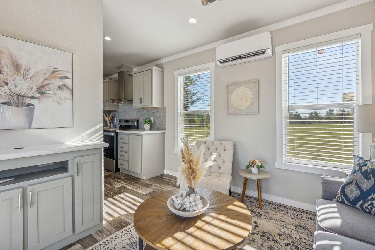 Bright living room with gray sofa, round wood table, large windows, and light decor.