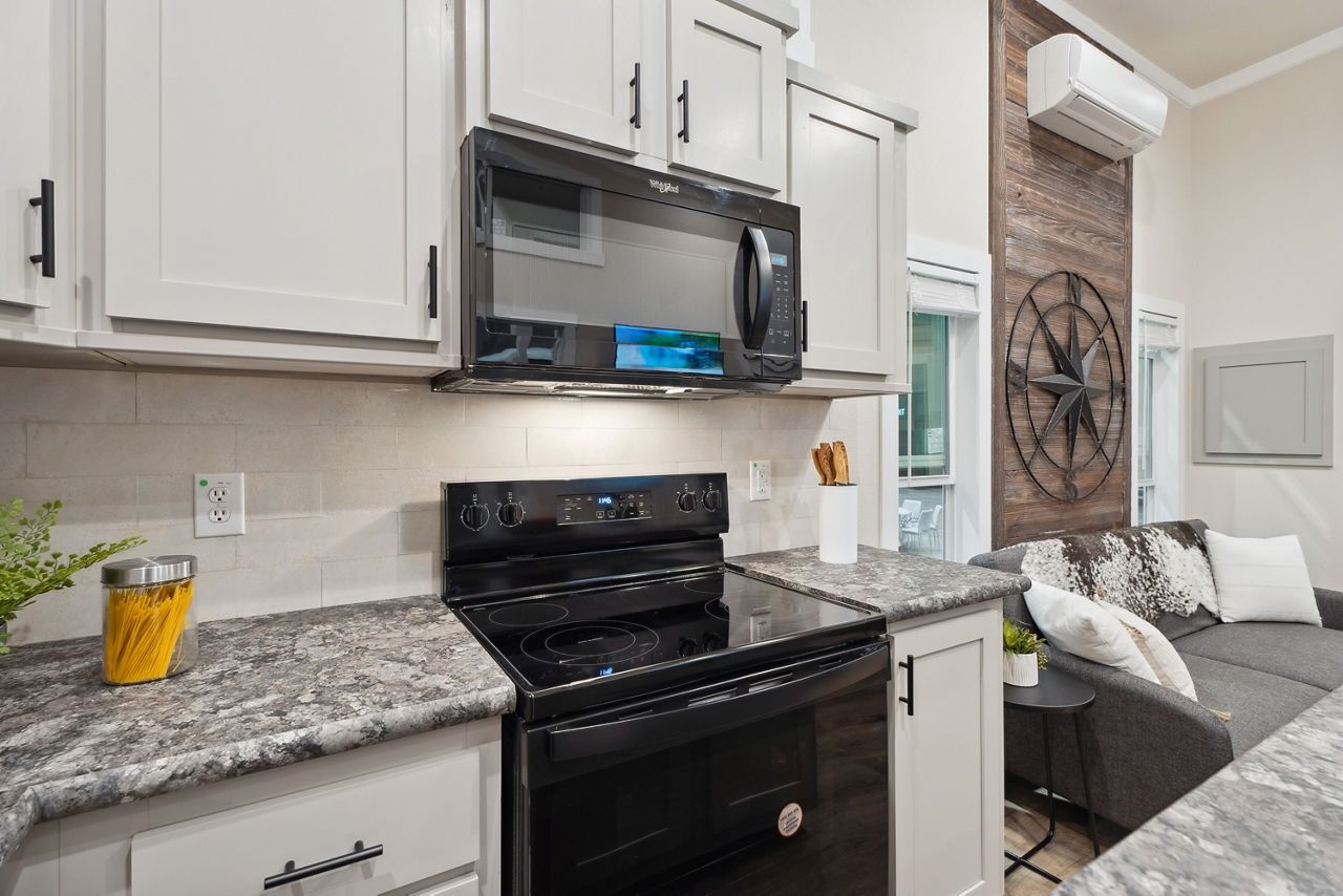 Modern kitchen with white cabinets, black stove, granite counters, and adjacent living room seating.