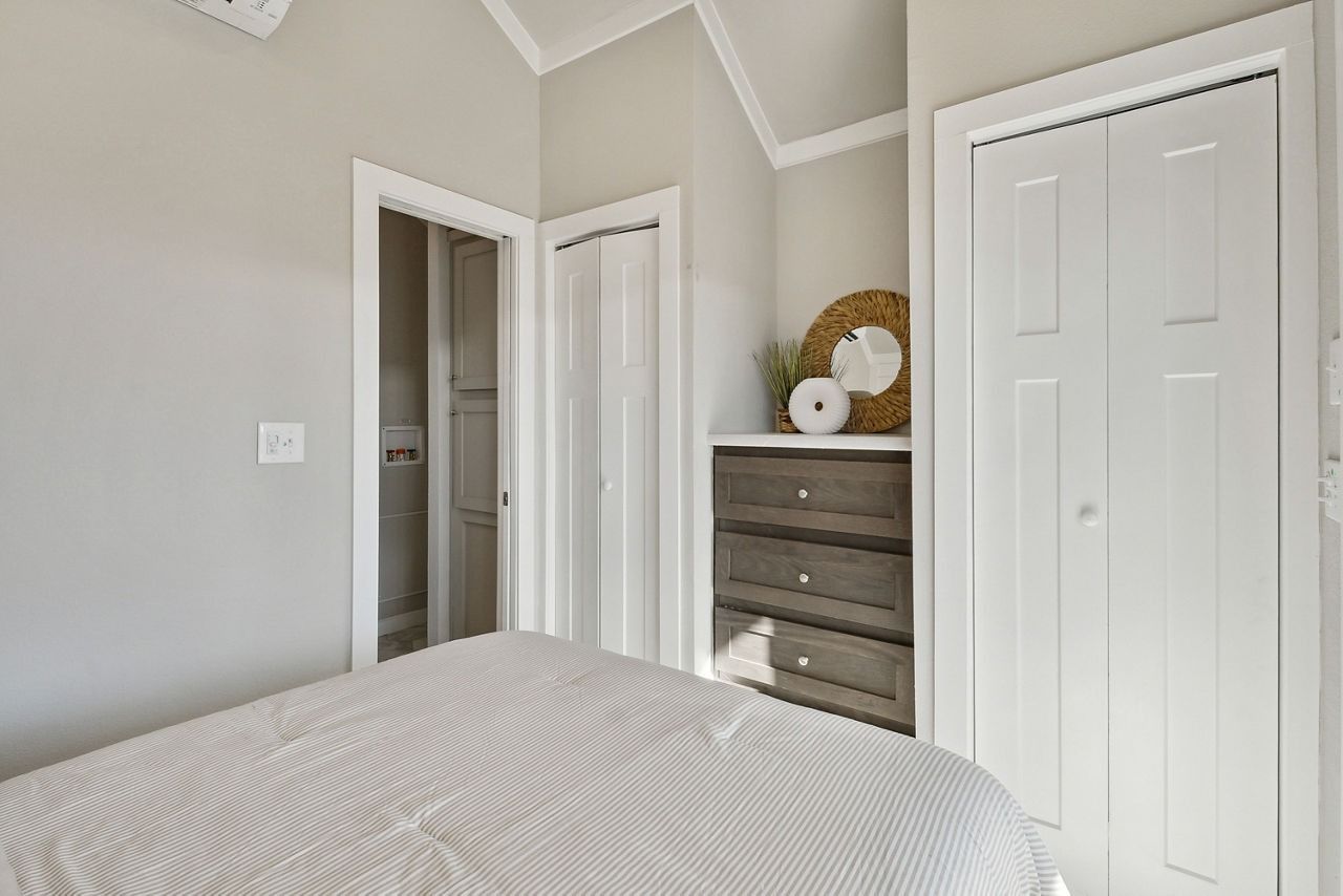 Bright bedroom with white bed, open closet, dresser, and decorative flowers on a shelf