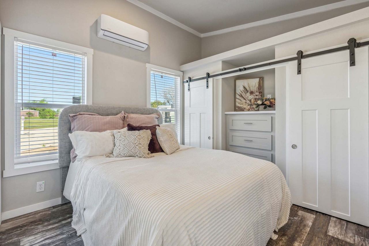 Bright bedroom with a white bed, sliding closet doors, dresser, and windows with blinds