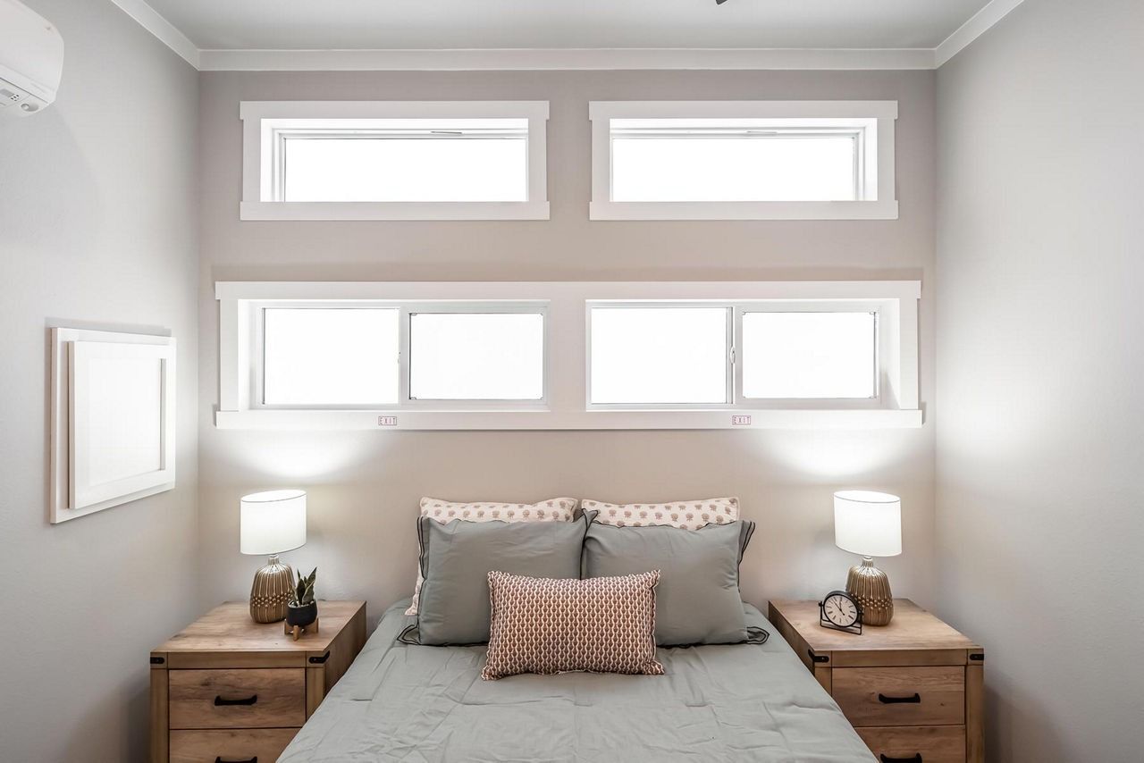 Bright bedroom with a bed, two bedside lamps, and windows above the headboard