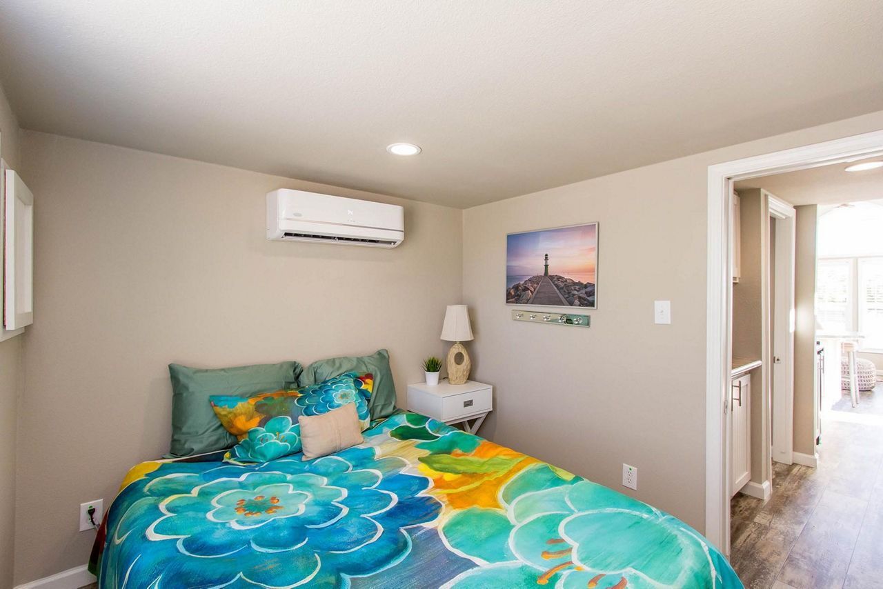 Bright bedroom with turquoise floral bedspread, wall art, nightstand, and doorway to hallway