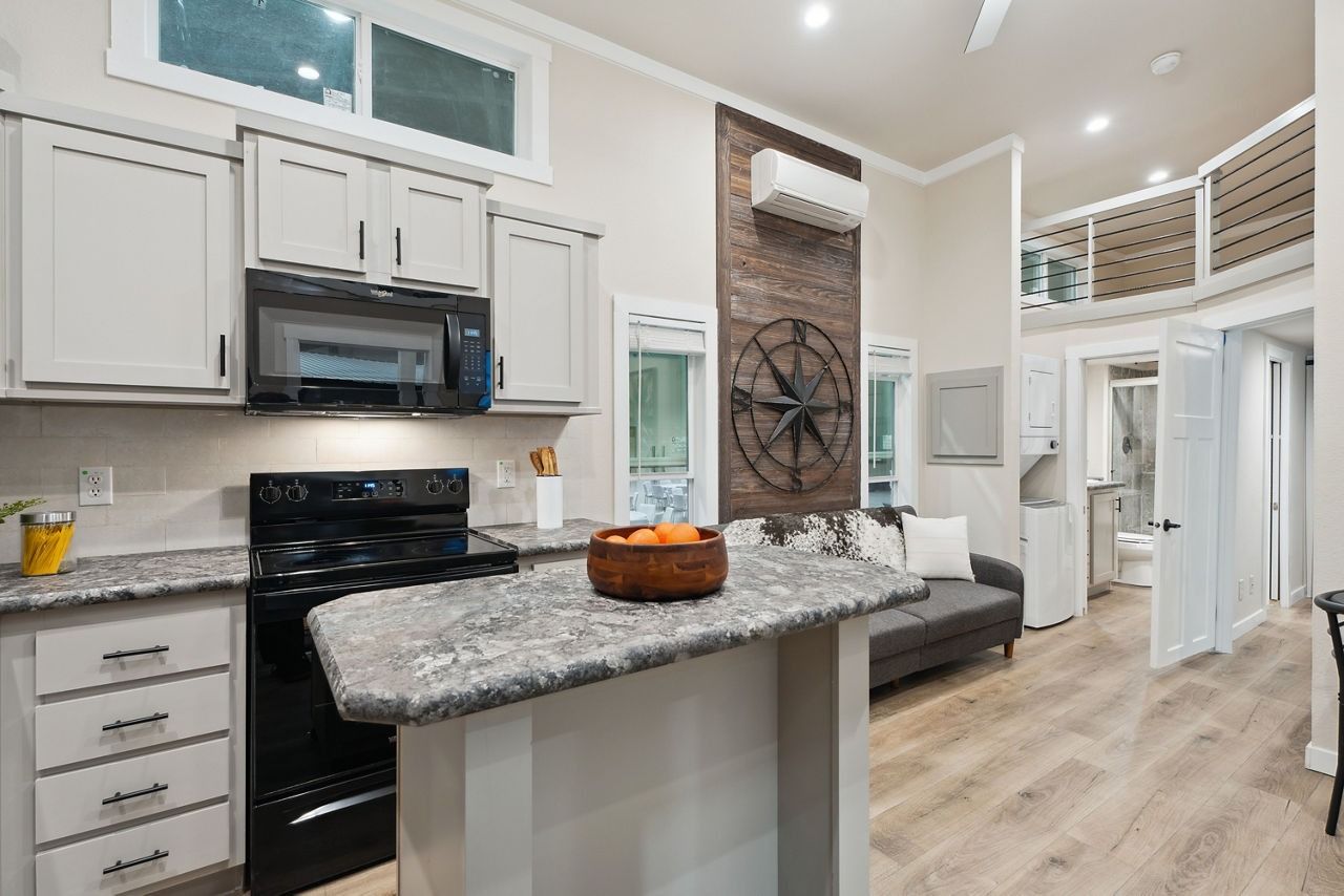 Bright kitchen with white cabinets, black appliances, granite island, and wood-look flooring