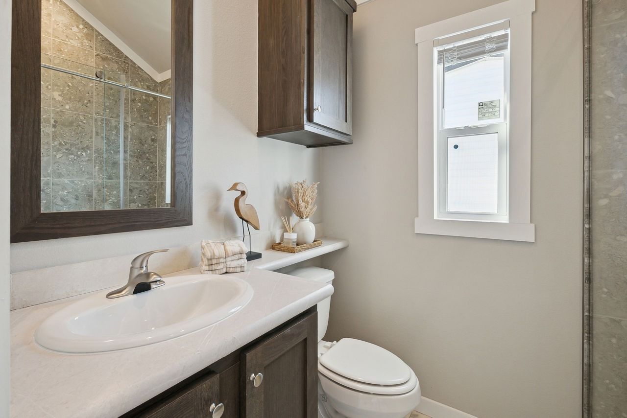 Small bathroom with vanity, sink, mirror, toilet, and window; dark cabinets and light walls.