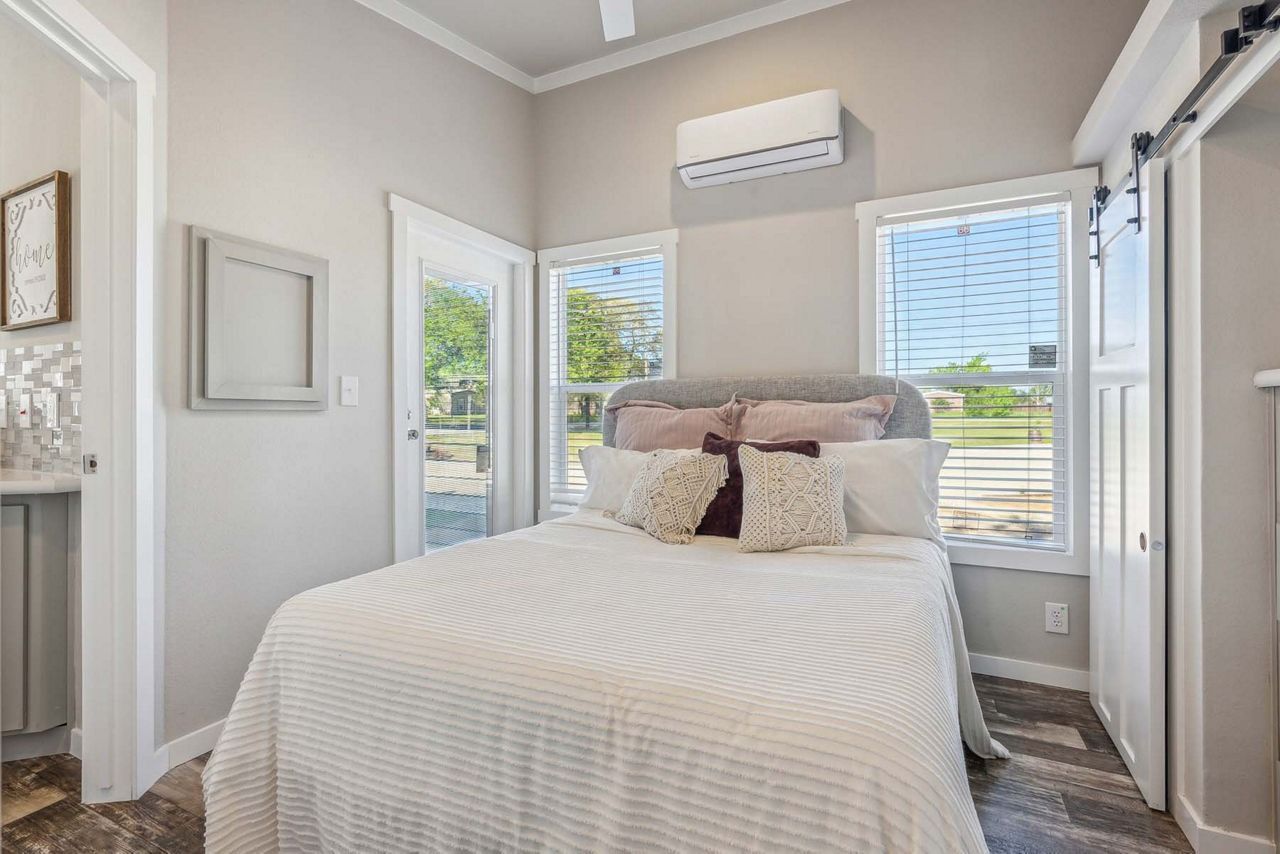 Bright bedroom with white bed, pillows, gray walls, and windows letting in natural light