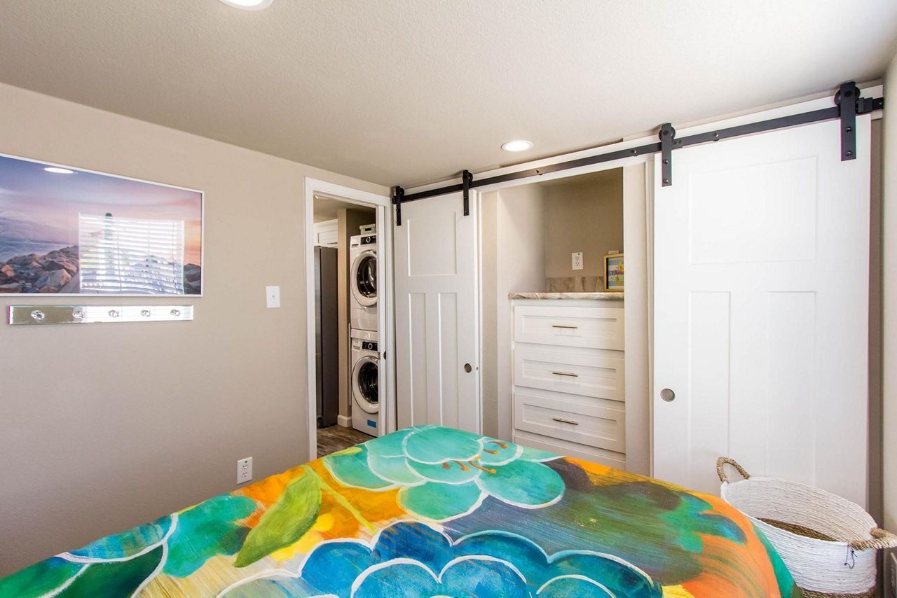 Bedroom with colorful quilt, sliding closet door, white dresser, and laundry nook.