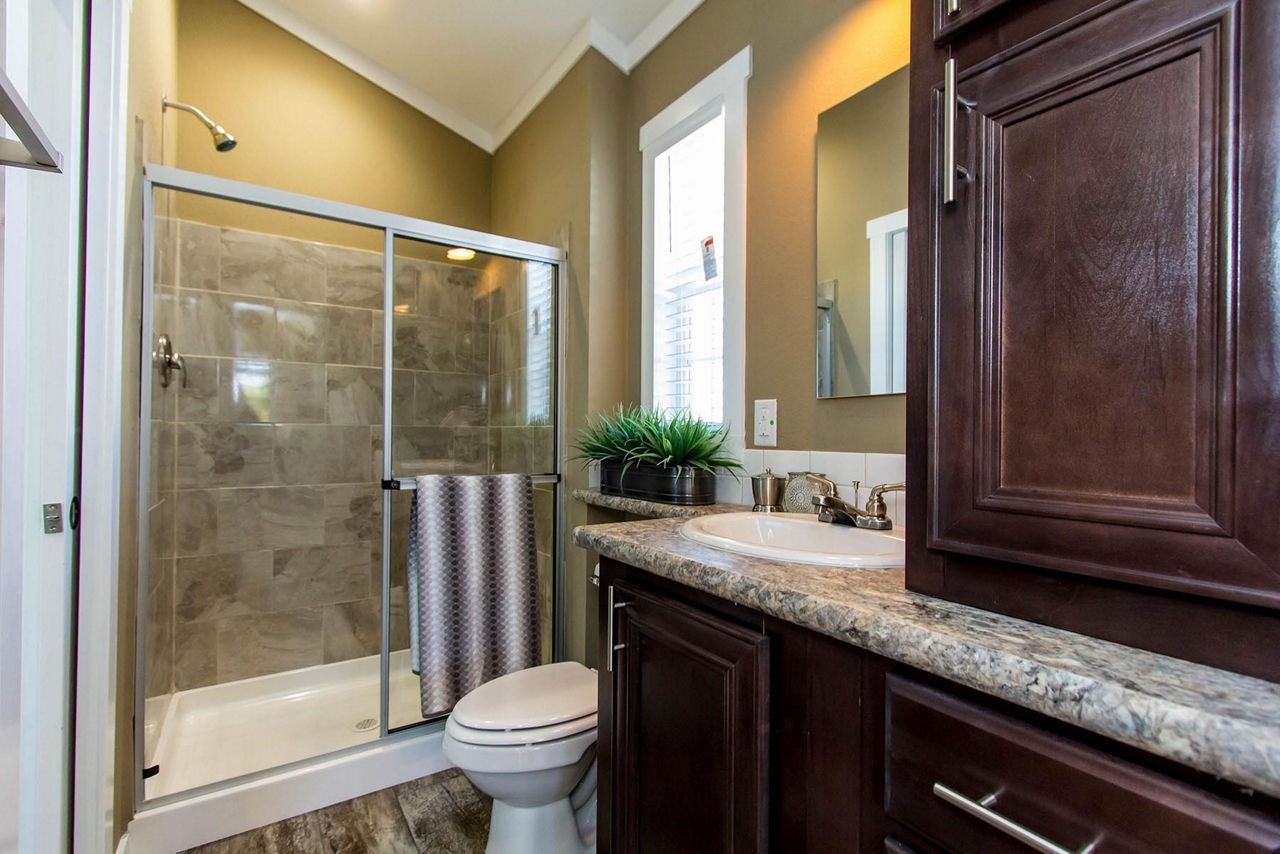 Bathroom with glass shower, toilet, and dark wood vanity with granite countertop.