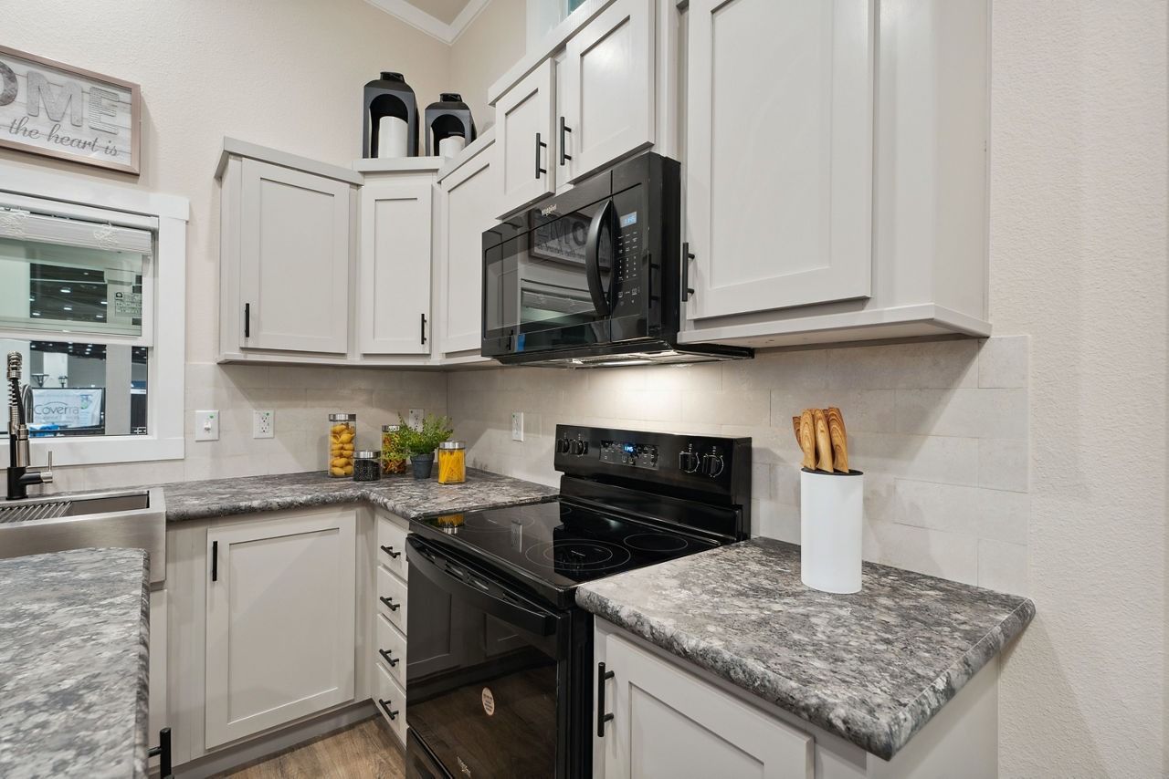 Compact white kitchen with black appliances, gray countertops, and cabinets along both walls.
