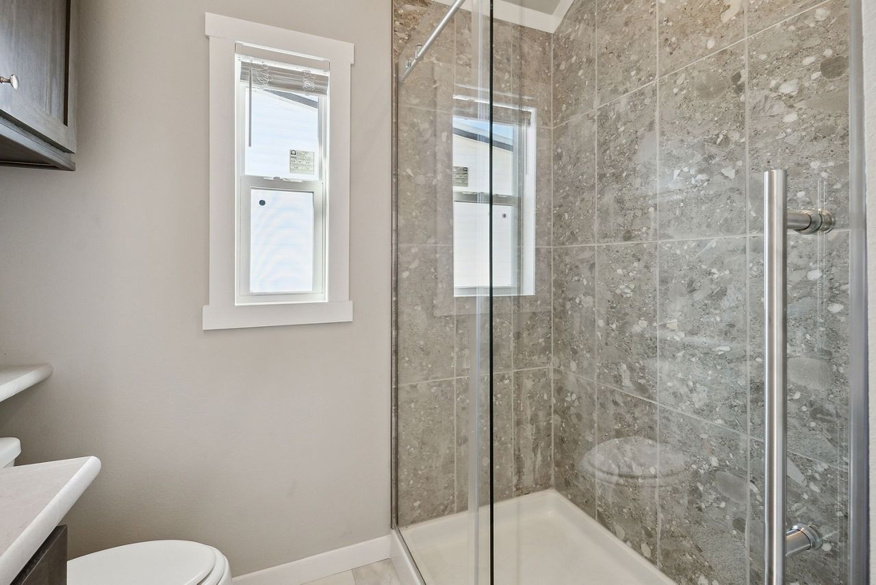 Small bathroom with glass shower, beige walls, and a white-framed window.