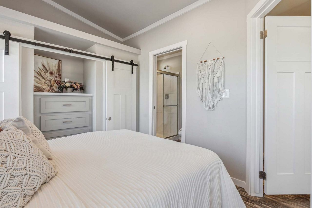 Bright bedroom with white bed, dresser, sliding barn door, and soft neutral decor