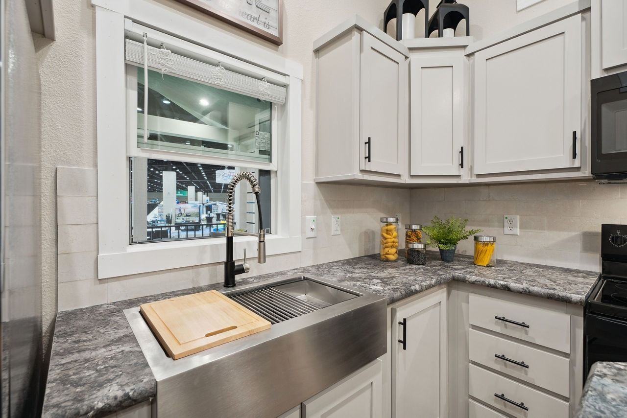 Bright kitchen sink with white cabinets, granite countertop, window, and cutting board near a black faucet
