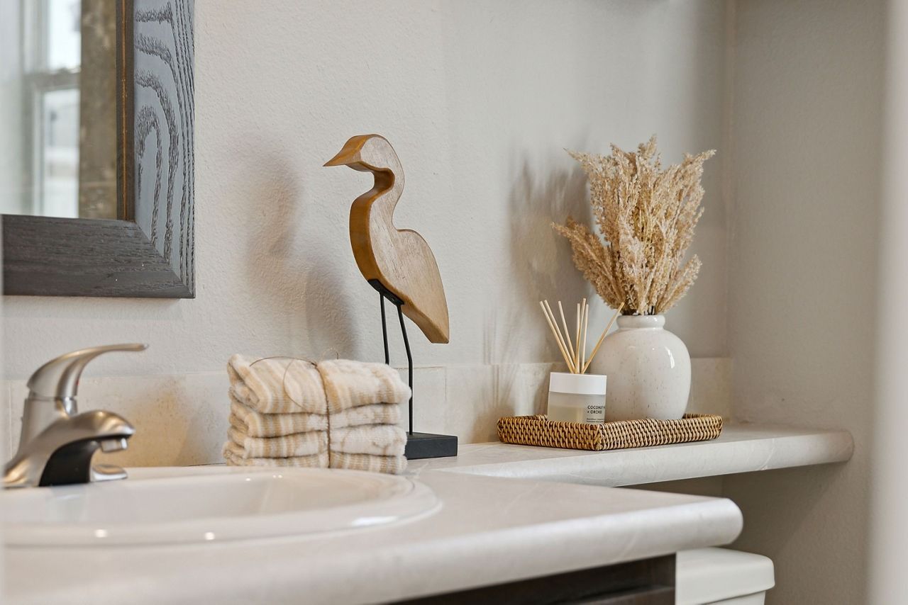 Bathroom sink with a white basin, gold faucet, bird figurine, towels, and dried flowers on a shelf.