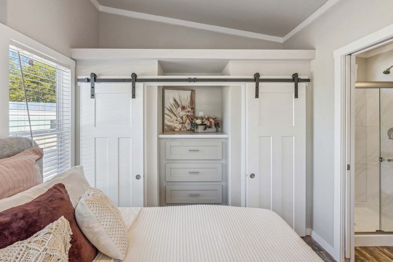 Bright bedroom with white barn doors, a dresser alcove, and a glass shower visible through the doorway