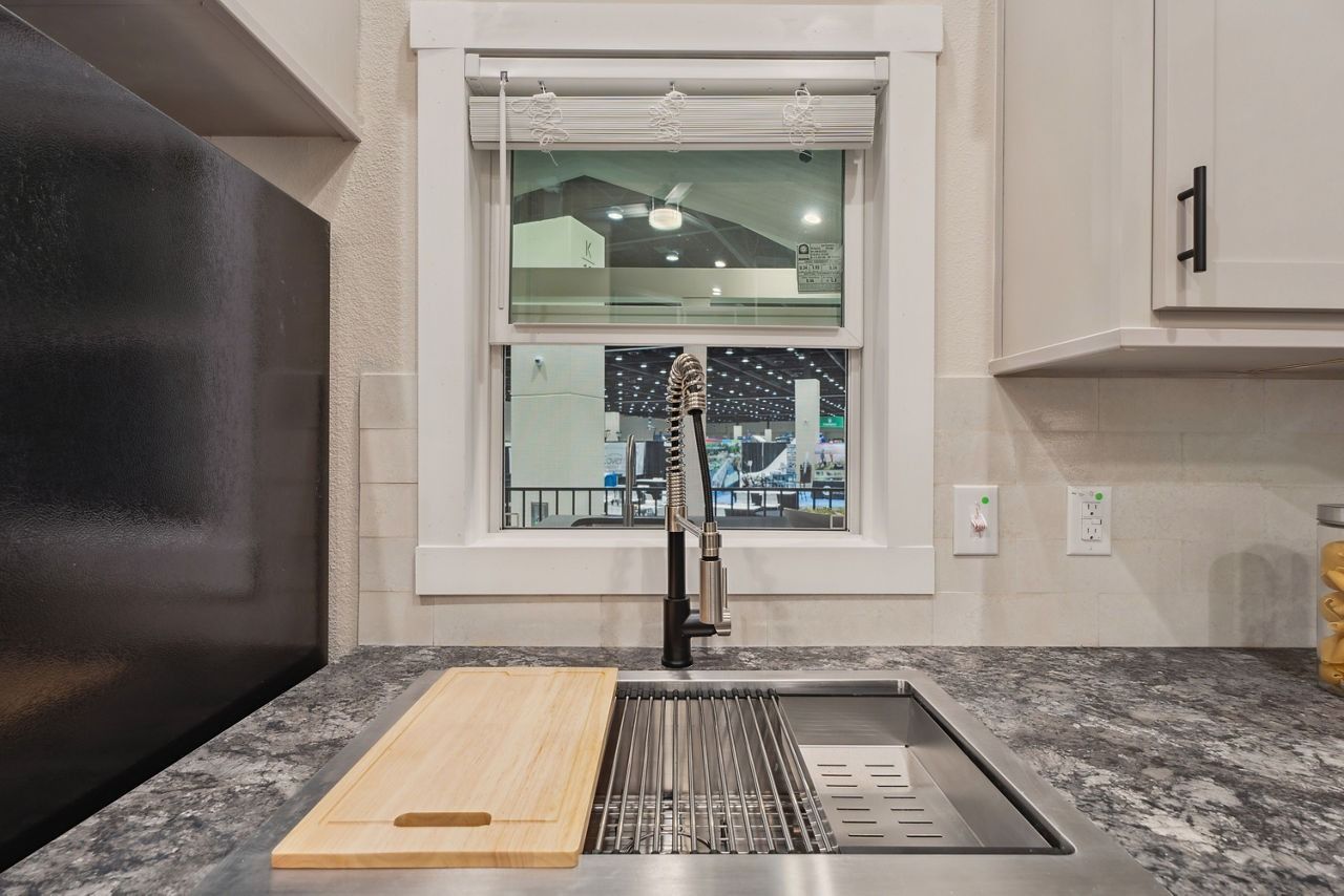 Modern kitchen sink with window view, wooden cutting board, and gray countertop cabinets