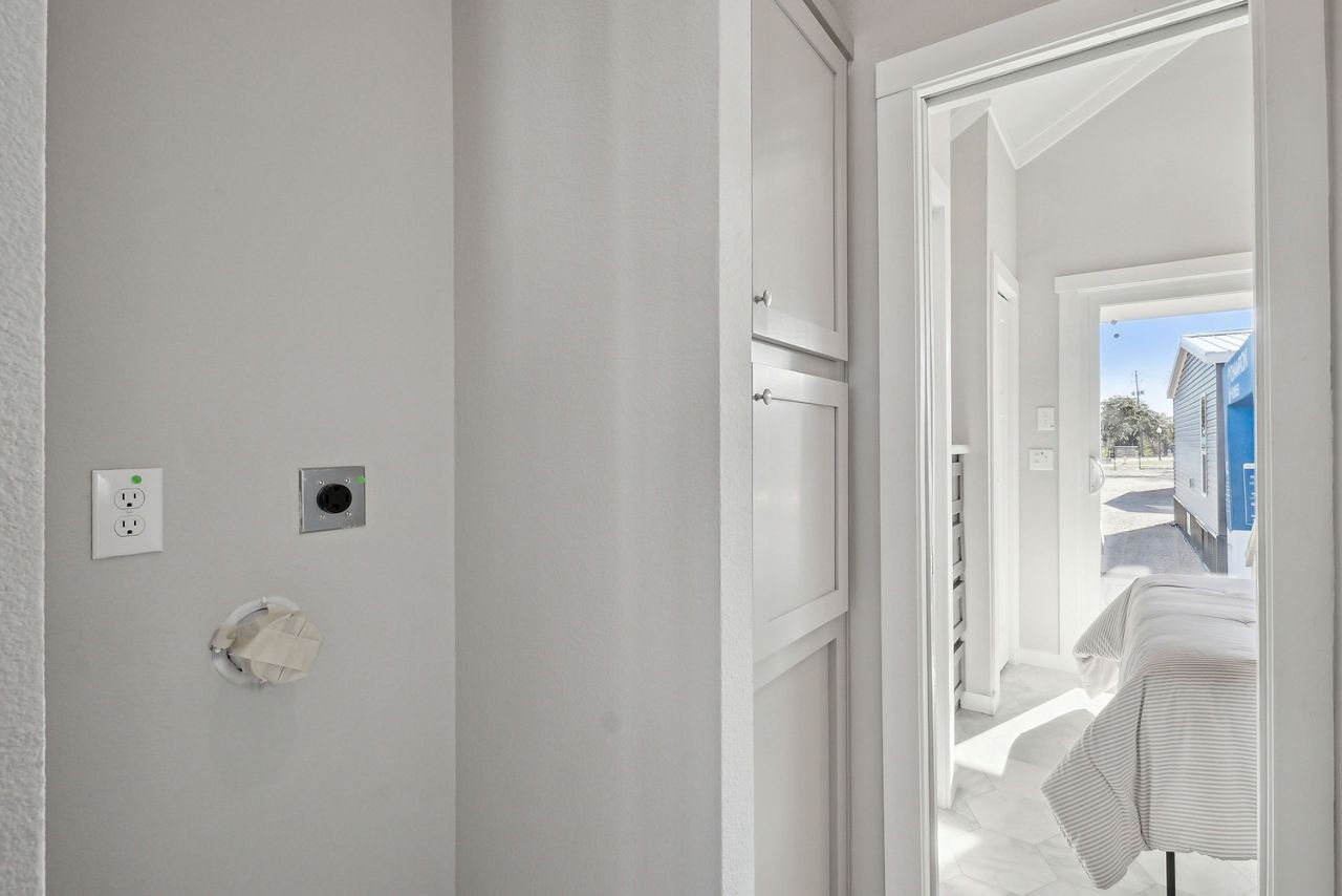 Bright hallway with white walls, a doorway to a sunny room, and a glimpse of a bed and snowy outdoor view