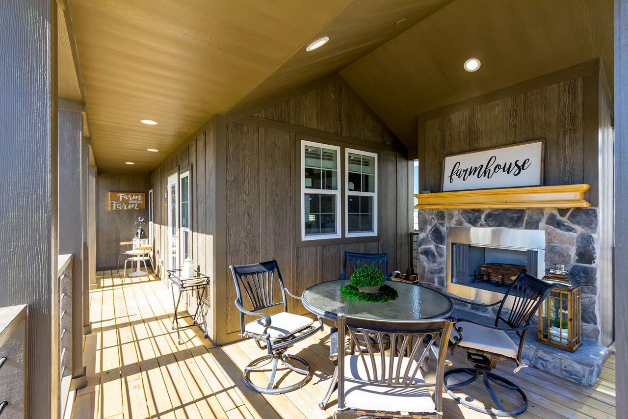 Covered patio with outdoor seating, stone fireplace, and wooden ceiling in a rustic setting