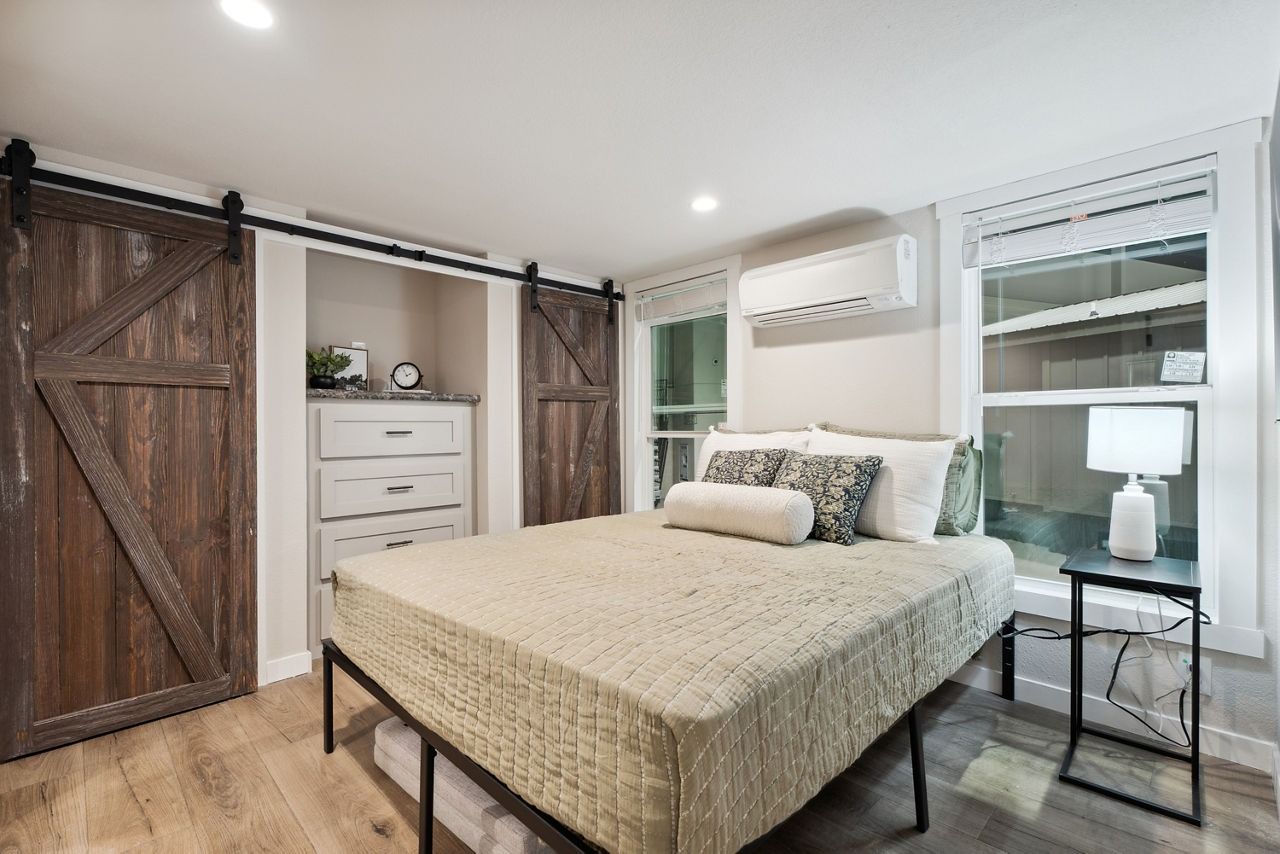 Modern bedroom with rustic barn doors, beige bedding, dresser, and bedside lamp