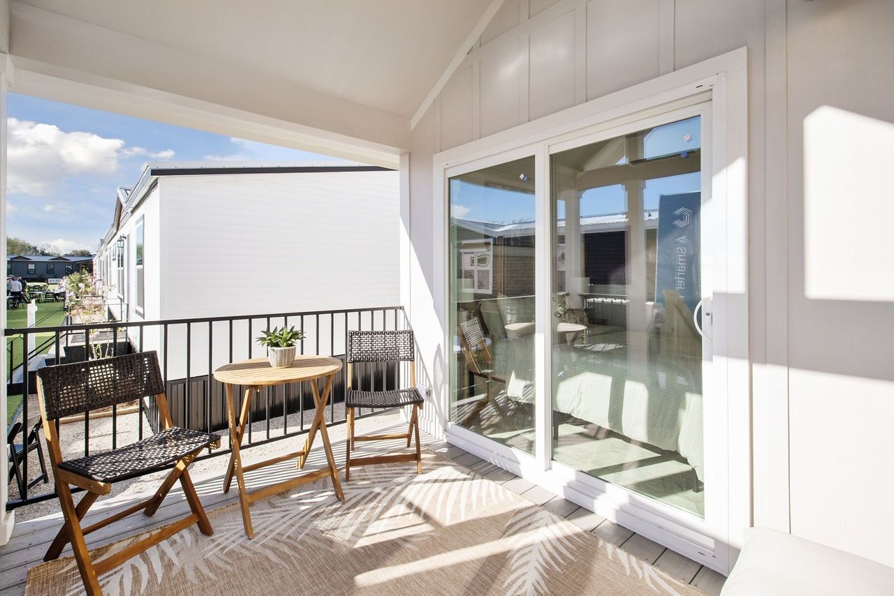 Balcony with wooden chairs, black railing, and sliding glass doors in bright sunlight