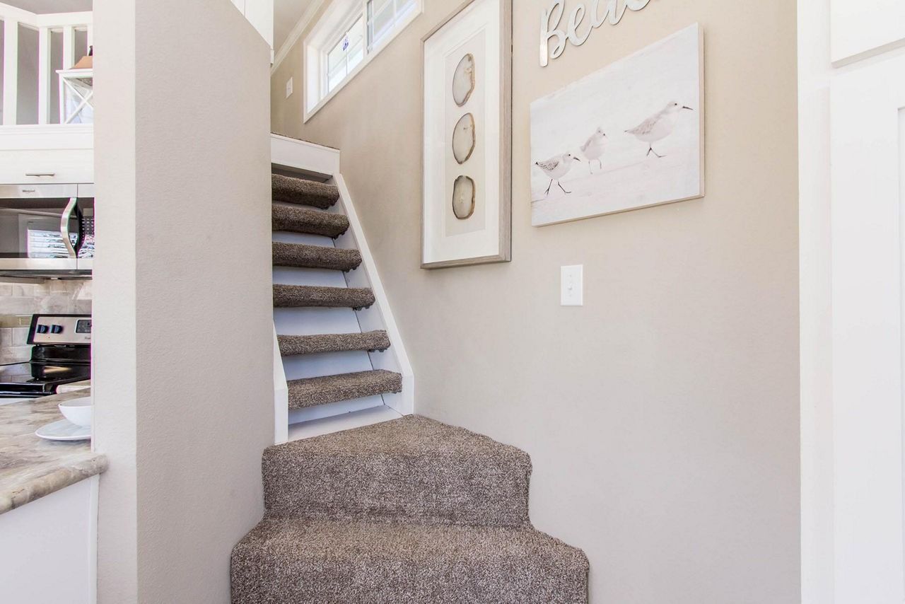 Carpeted staircase in a beige hallway with framed wall art and white trim
