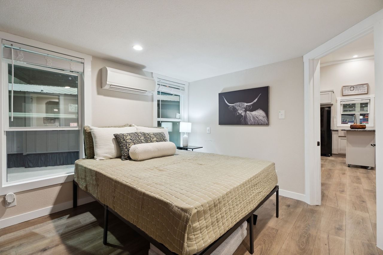 Bright bedroom with a bed, wall art, windows, and an open doorway to a bathroom