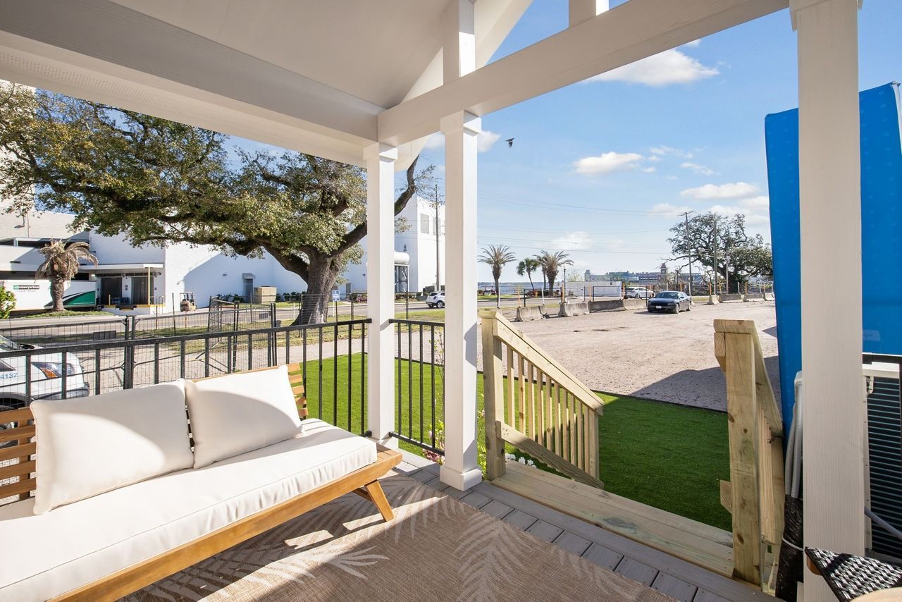 Covered porch with white sofa overlooking a sunny beach and boardwalk
