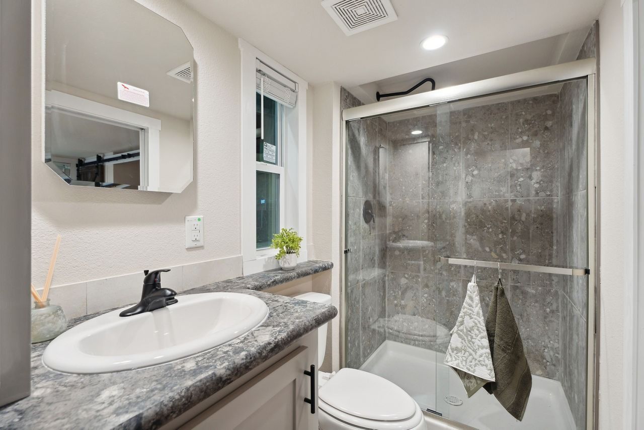Small modern bathroom with vanity sink, mirror, toilet, and glass shower enclosure