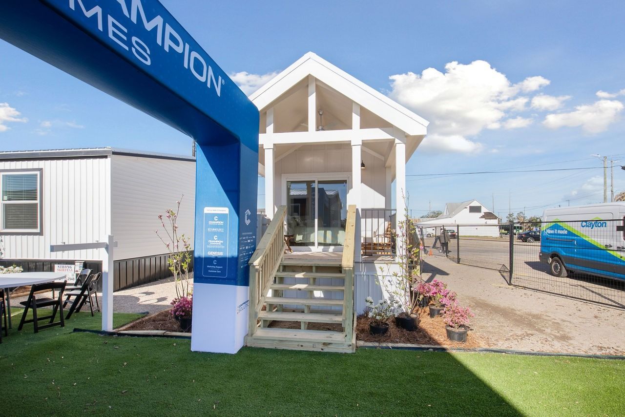 Small white beach hut under blue canopy beside a gravel path and parked beach trailers.