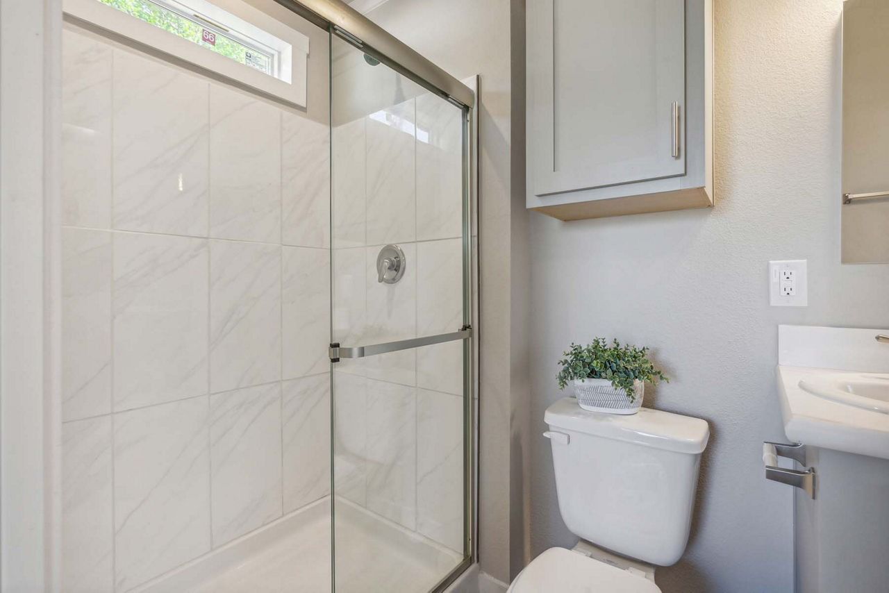 Small bathroom with a glass shower, toilet, and wall cabinet in neutral tones