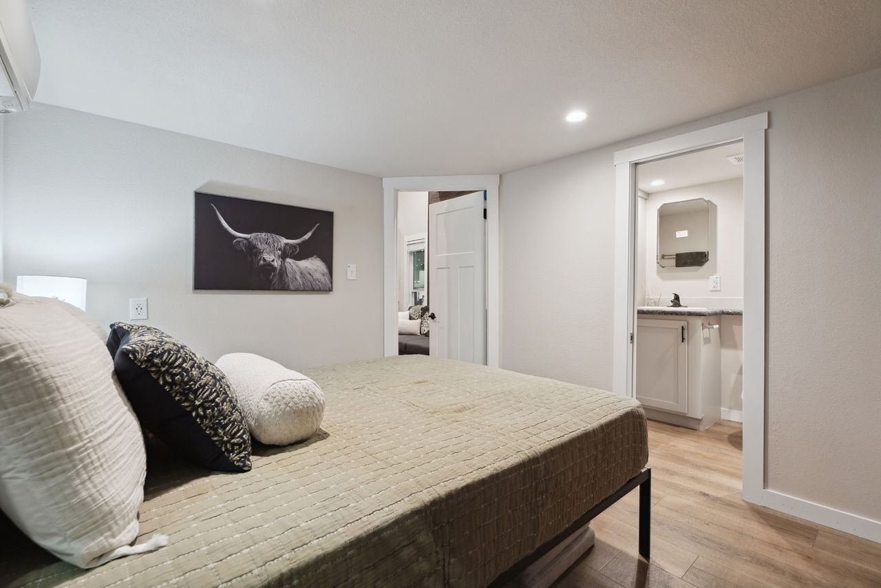 Bright bedroom with a made bed, wall art, and an ensuite bathroom visible through open doors.