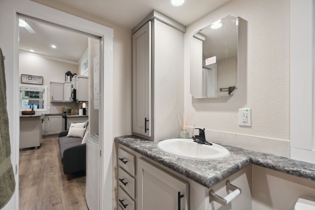 Hallway bathroom vanity with granite counter and mirror, opening to a bedroom in the background