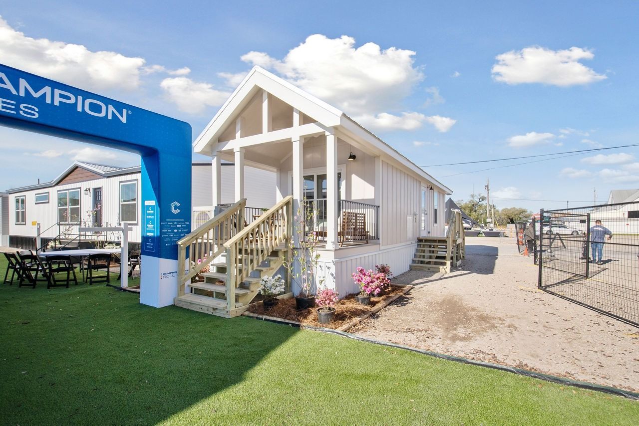 Small white house display with porch steps and blue Champion arch at a park or fairground