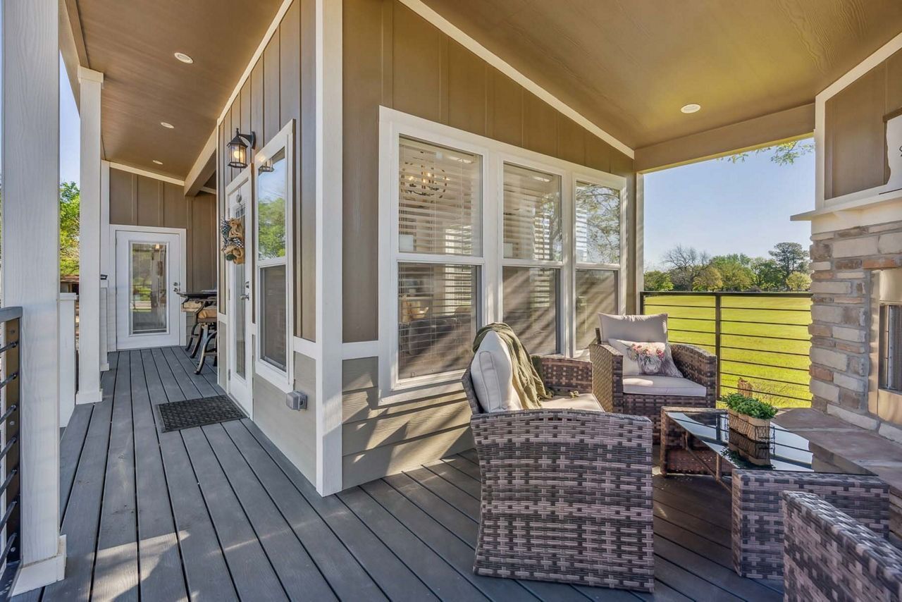 Covered porch with wicker chairs, stone columns, and a view of green lawn through white French doors