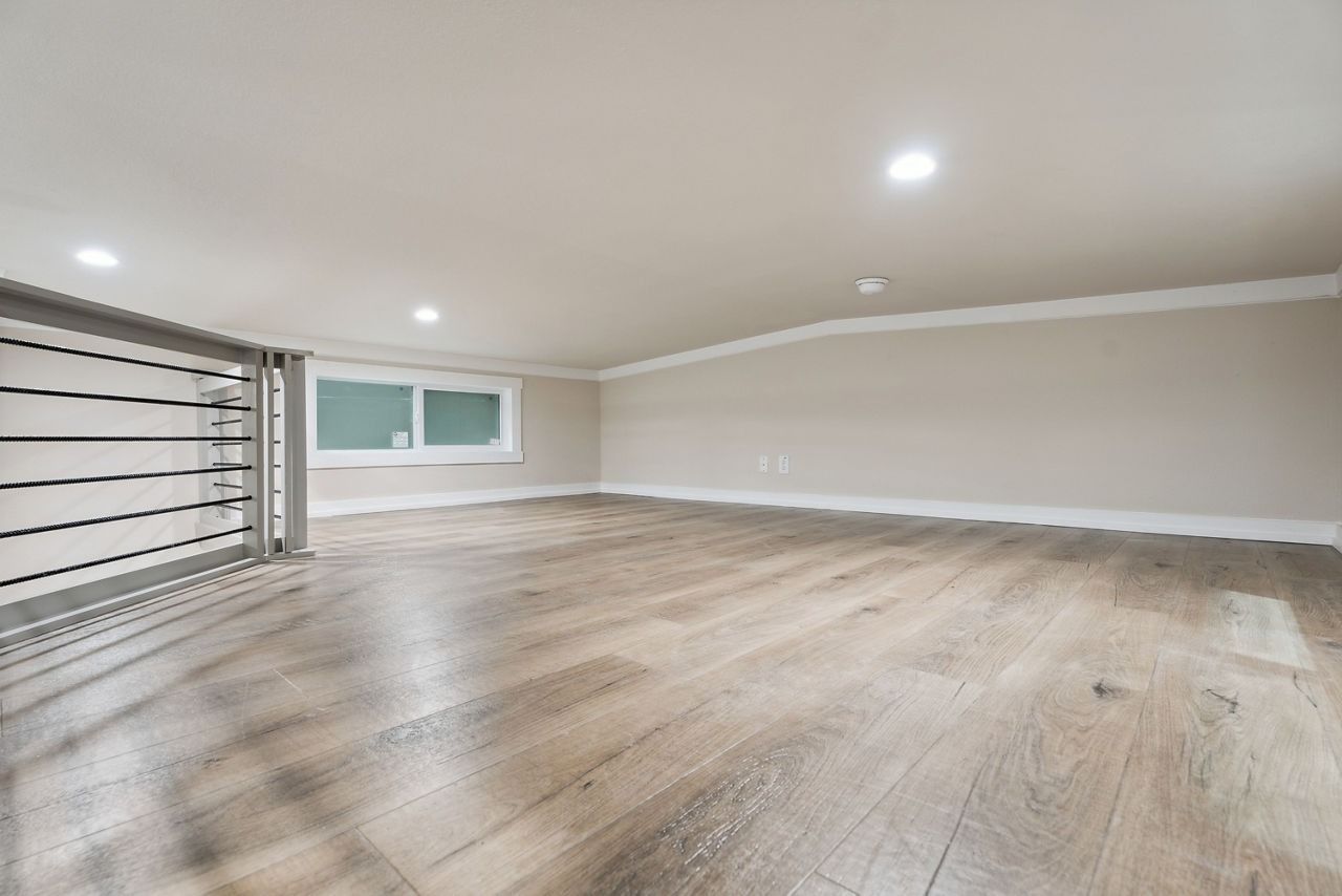 Empty modern room with light wood floors, recessed lights, and a small window on the far wall
