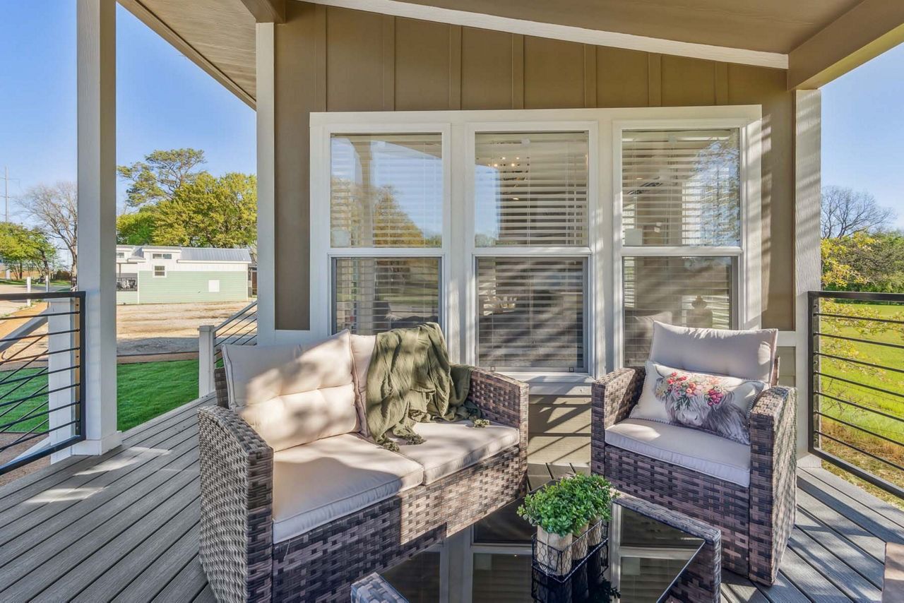 Covered porch with wicker seating, patterned cushions, and a small table overlooking a grassy yard.