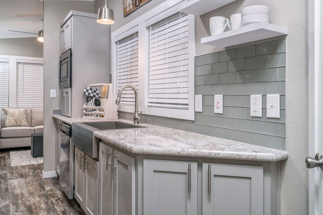 Modern kitchen with gray cabinets, marble countertops, white shutters, and light green tile backsplash